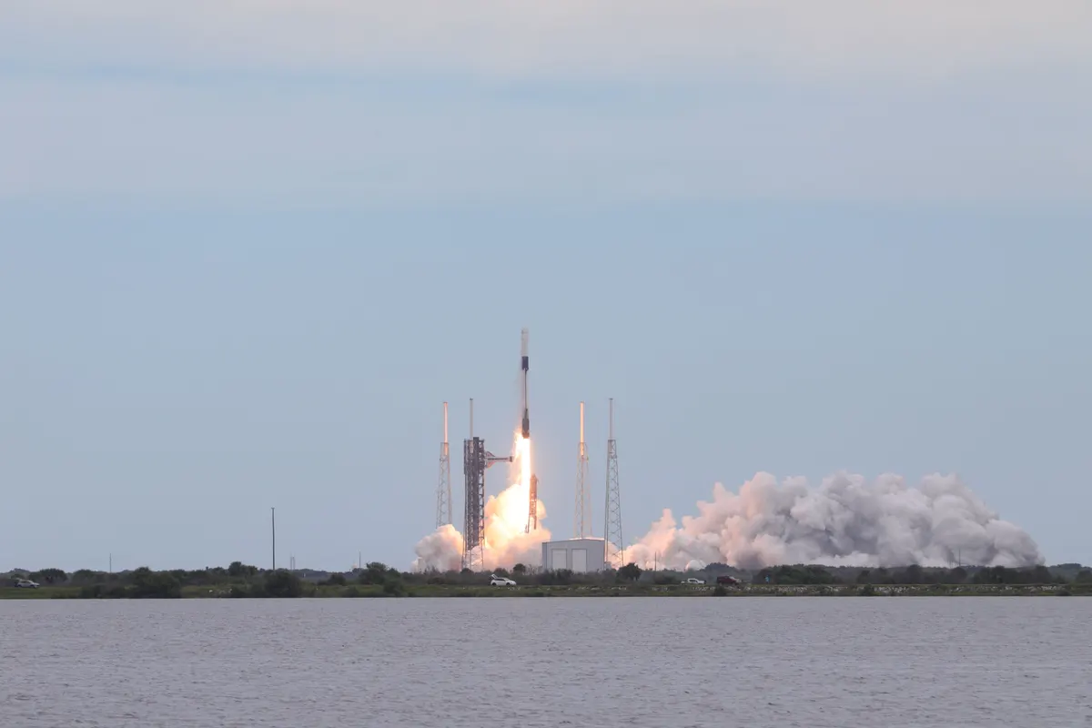 A Falcon 9 rocket lifting off from Cape Canaveral with a plume of white smoke across the water
