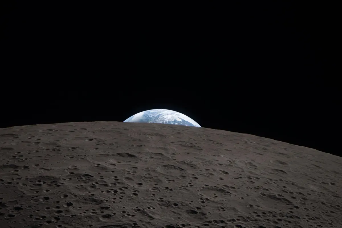Earth setting behind the grey, cratered horizon of the Moon