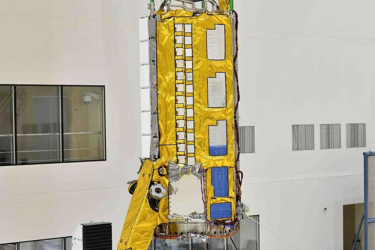 Engineers using a crane to lift the yellow-wrapped radar payload of the NISAR satellite in a clean room
