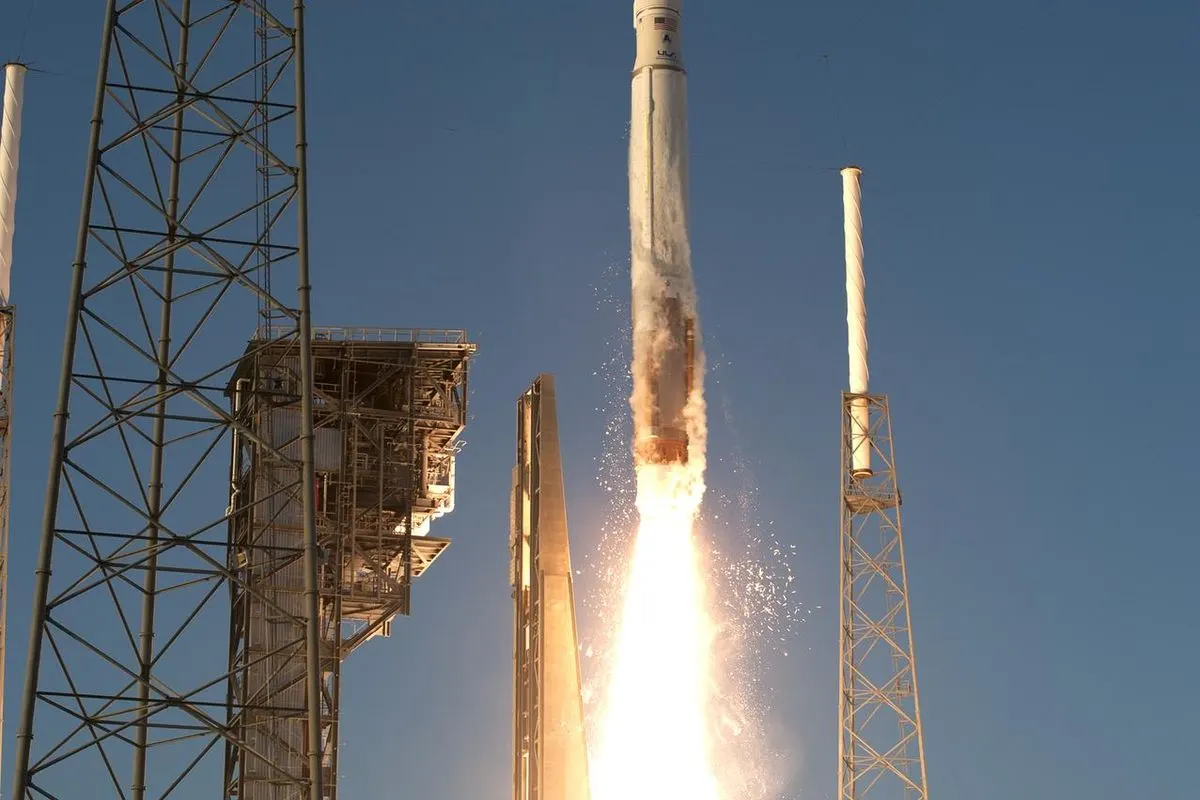 An Atlas V rocket lifting off with bright orange flames beside a launch tower