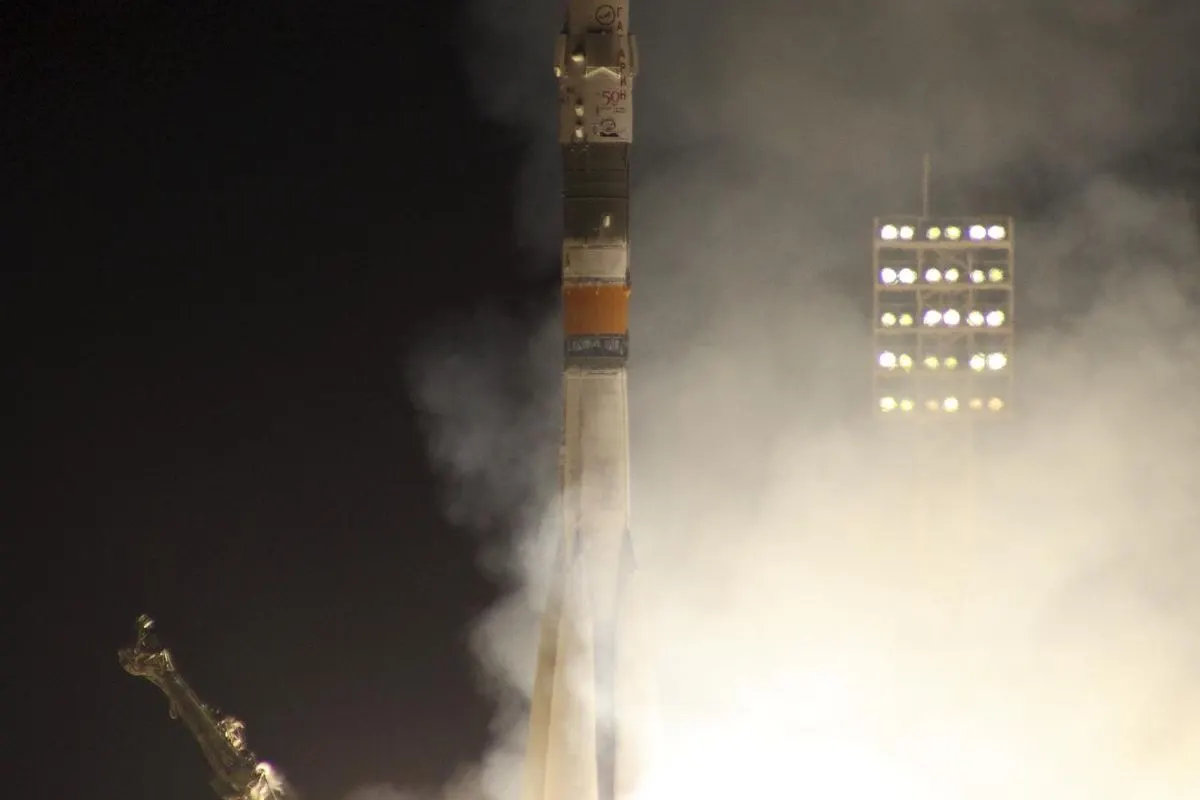 A Soyuz rocket lifting off at night, lit by its own exhaust, with a service tower beside it
