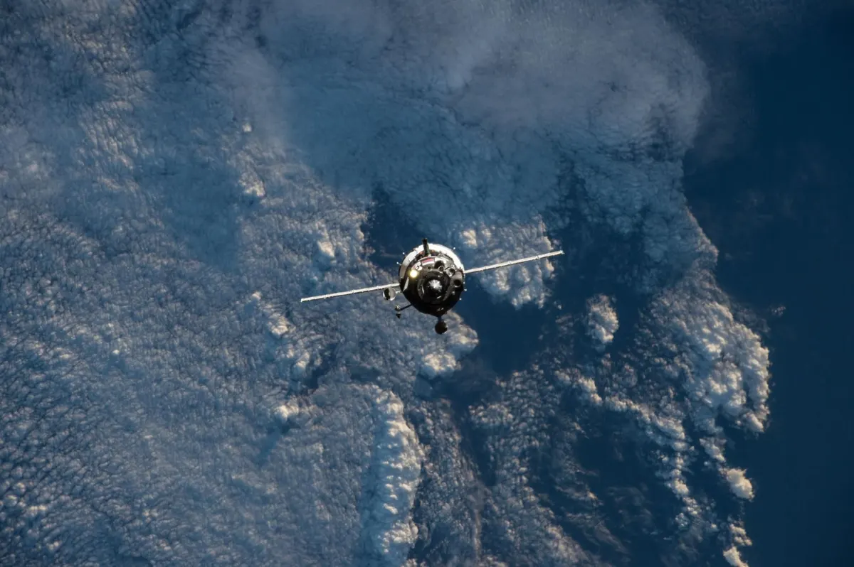 A Soyuz spacecraft approaching the International Space Station above Earth's clouds