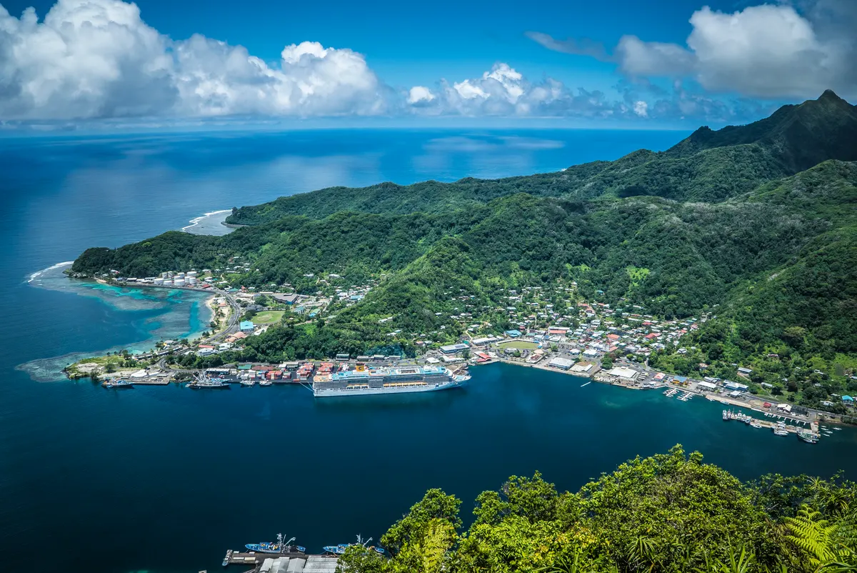A town and harbor on a green, mountainous island in American Samoa, seen from above